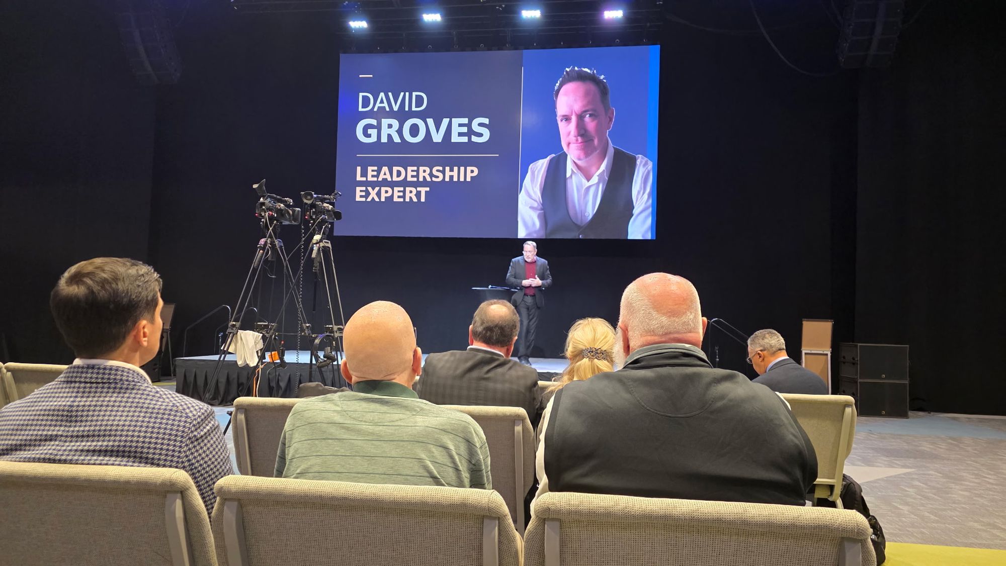 Leaders in the audience watching Dave Groves speak, with cameras recording the session